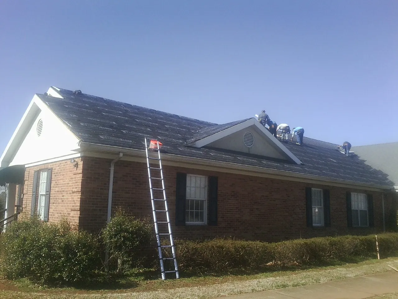 Crew tearing shingles off a brick ranch roof with a ladder set — Metal Roof Repair work by our crew in Hunt