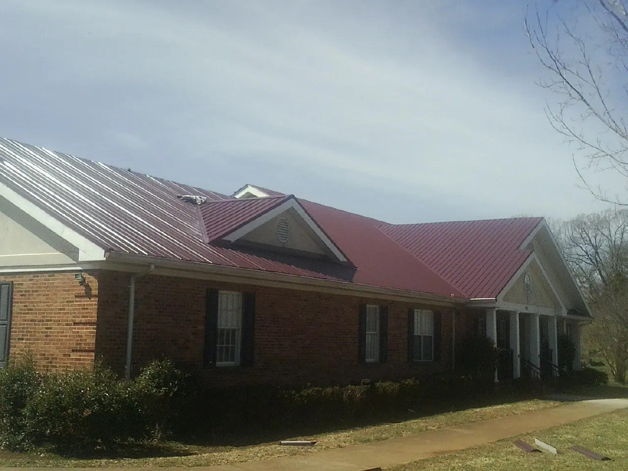 Red metal roof with gabled entries on a long brick building, from a Hail Damage Roof Repair job in Hunt