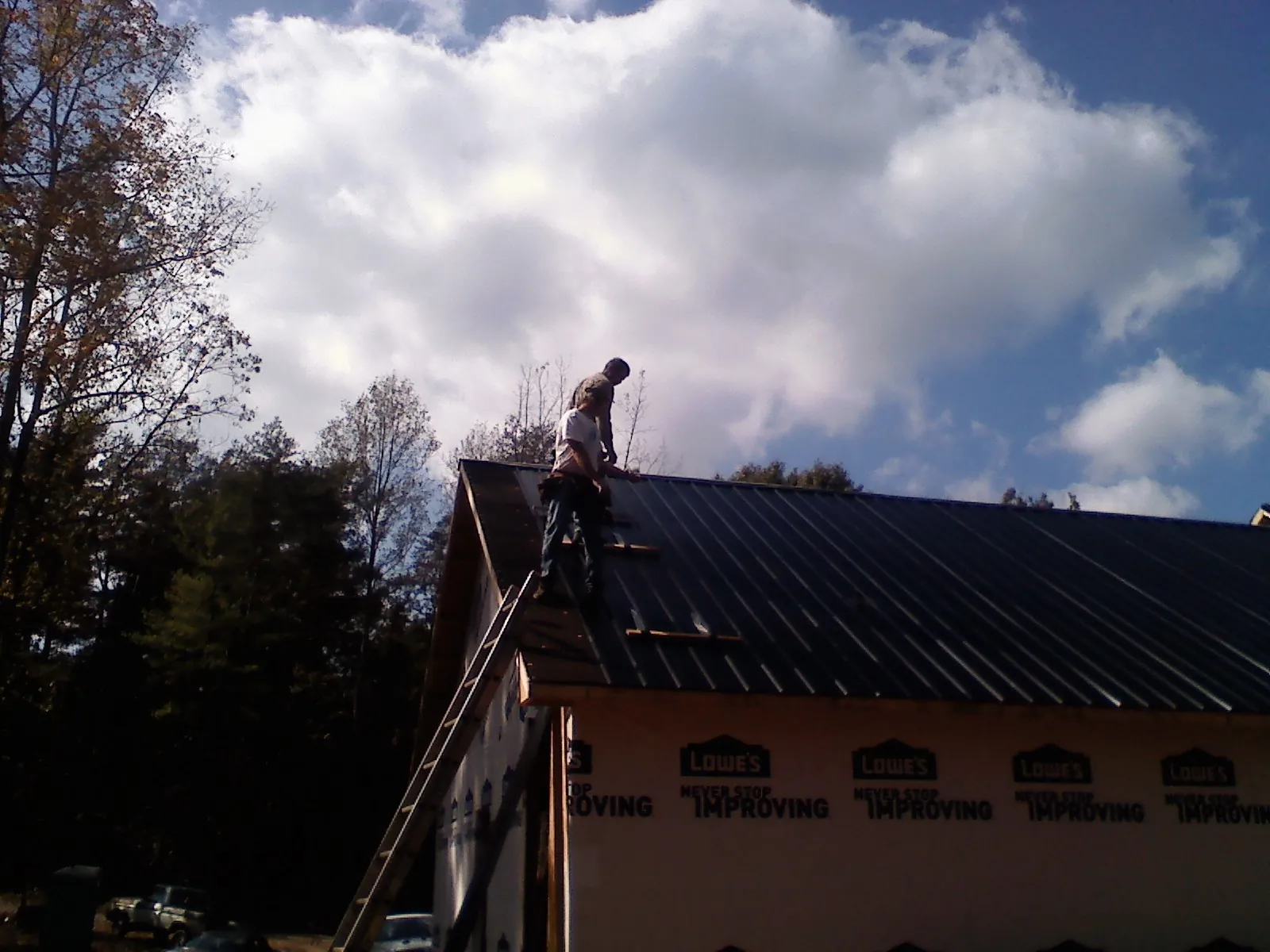 Roofer fastening dark metal panels high against a cloudy sky, from a Roof Inspection job in Hunt