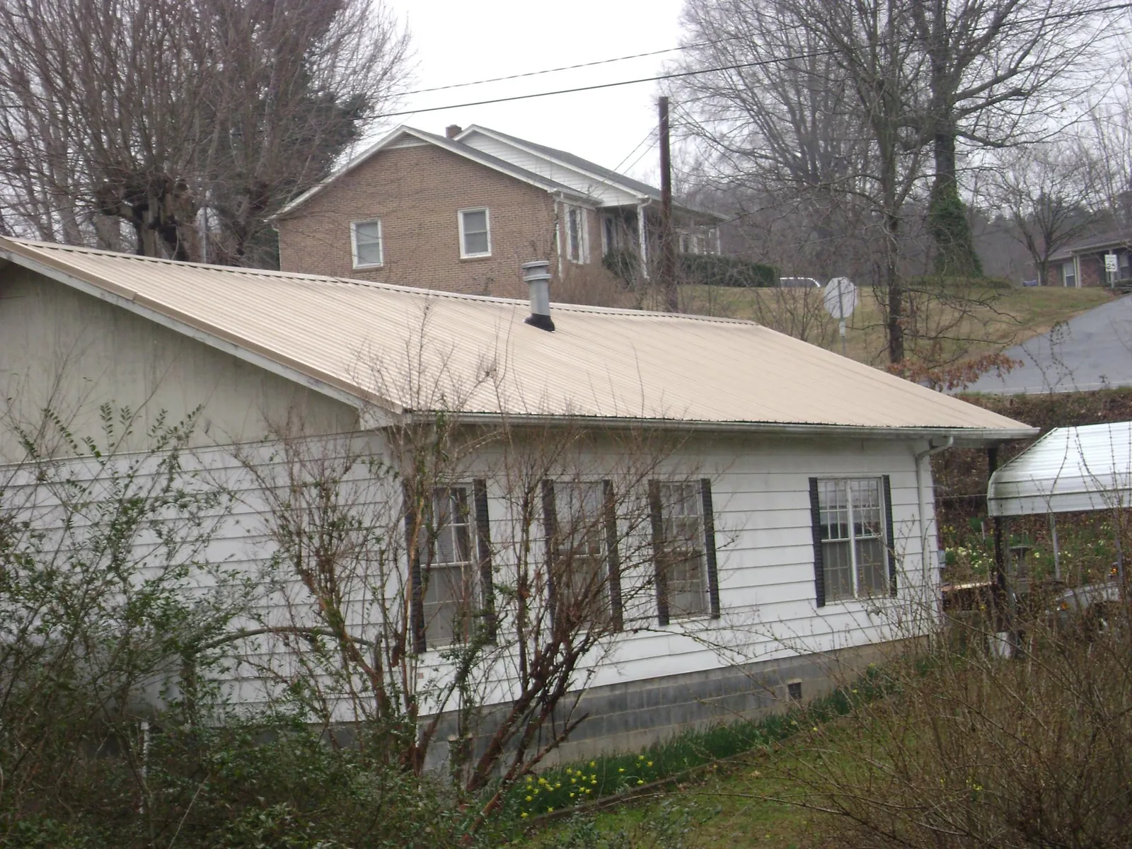 Tan metal roof on a white sided house set into a hillside — Commercial Roofing by Roofing Brothers in Hunt