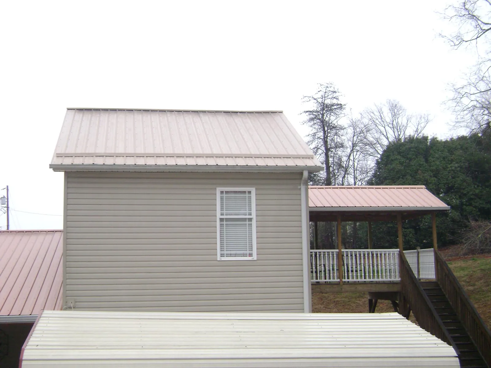 Tan metal roofs on a two story addition and attached porch, from a Roof Replacement job in Hunt